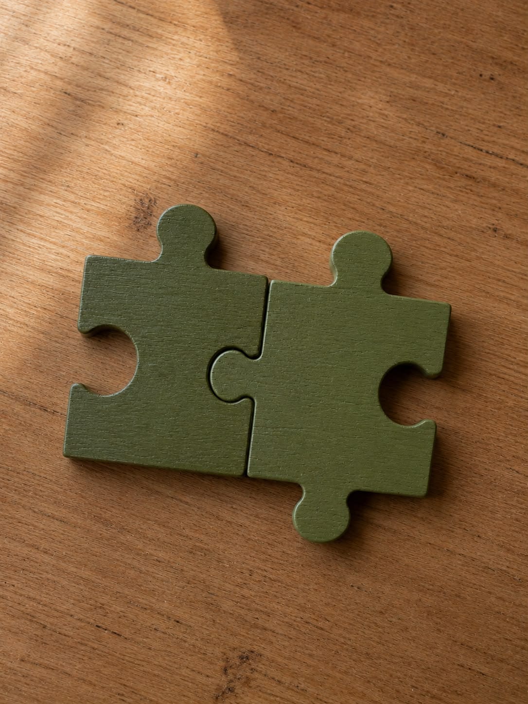 Zwei ineinandergreifende grüne Puzzleteile auf einem Holztisch